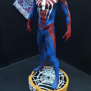 May include: A red and blue Spider-Man action figure with a white spider symbol on the chest. The figure is standing on a round base with a spider web design and the words "Spider-Man" printed on the front.