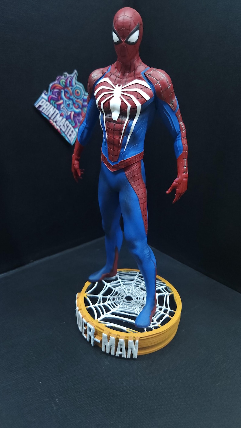 May include: A red and blue Spider-Man action figure with a white spider symbol on the chest. The figure is standing on a round base with a spider web design and the words "Spider-Man" printed on the front.