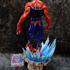 Op de afbeelding: Een gedetailleerd beeld van Spider-Man, van achteren gezien, met zijn iconische rood-blauwe pak. De figuur is dynamisch geposeerd, met een waterachtig effect als basis. Het beeld staat op een rotsachtige basis met het Printmaster-logo.