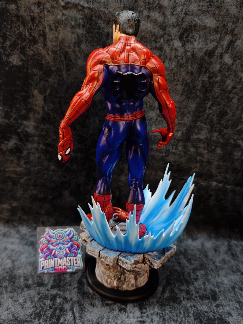 Op de afbeelding: Een gedetailleerd beeld van Spider-Man, van achteren gezien, met zijn iconische rood-blauwe pak. De figuur is dynamisch geposeerd, met een waterachtig effect als basis. Het beeld staat op een rotsachtige basis met het Printmaster-logo.