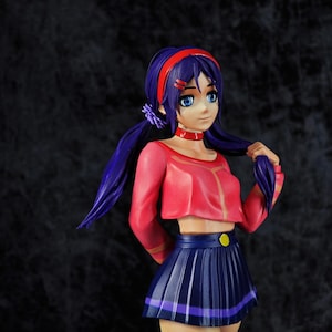 May include: A figurine of a female anime character with blue eyes and purple hair styled in pigtails. She wears a red headband, choker, and long-sleeved crop top. Her pleated skirt is navy blue, and she has striped thigh-high socks. A yellow button accents the skirt.