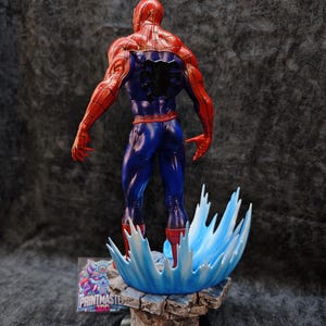 Op de afbeelding: Een gedetailleerd beeldje van Spider-Man, van achteren gezien, in zijn rood-blauwe kostuum. Het beeldje staat op een rotsachtige basis met een blauw watereffect. De basis heeft een logo "PRINTMASTER 3DD".