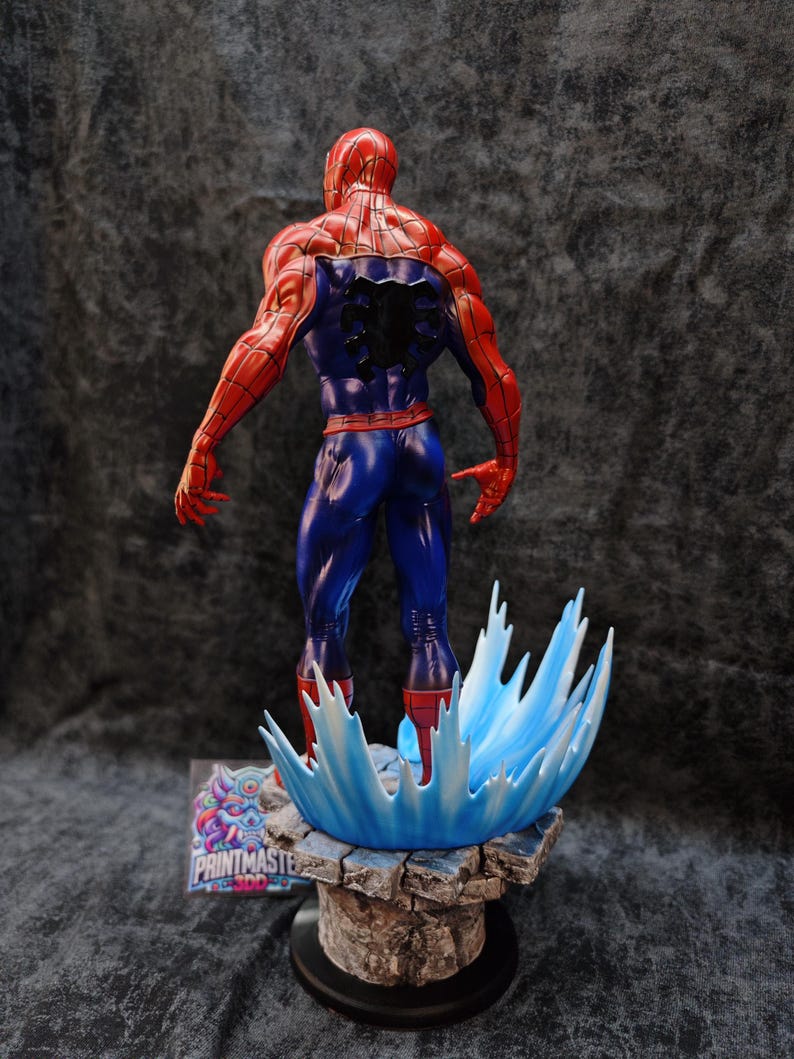 Op de afbeelding: Een gedetailleerd beeldje van Spider-Man, van achteren gezien, in zijn rood-blauwe kostuum. Het beeldje staat op een rotsachtige basis met een blauw watereffect. De basis heeft een logo "PRINTMASTER 3DD".