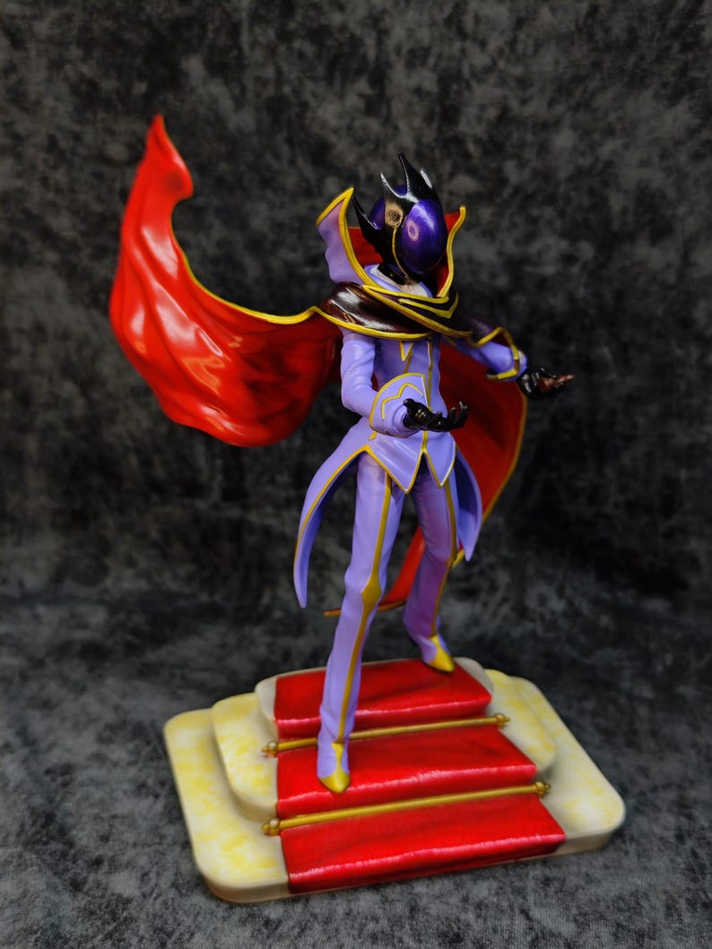 Pu&ograve; includere: Statuetta di un personaggio in un completo viola e oro con un mantello rosso. La figura &egrave; in piedi su una piattaforma con moquette rossa con finiture dorate. Il personaggio ha un elmo con una visiera viola.