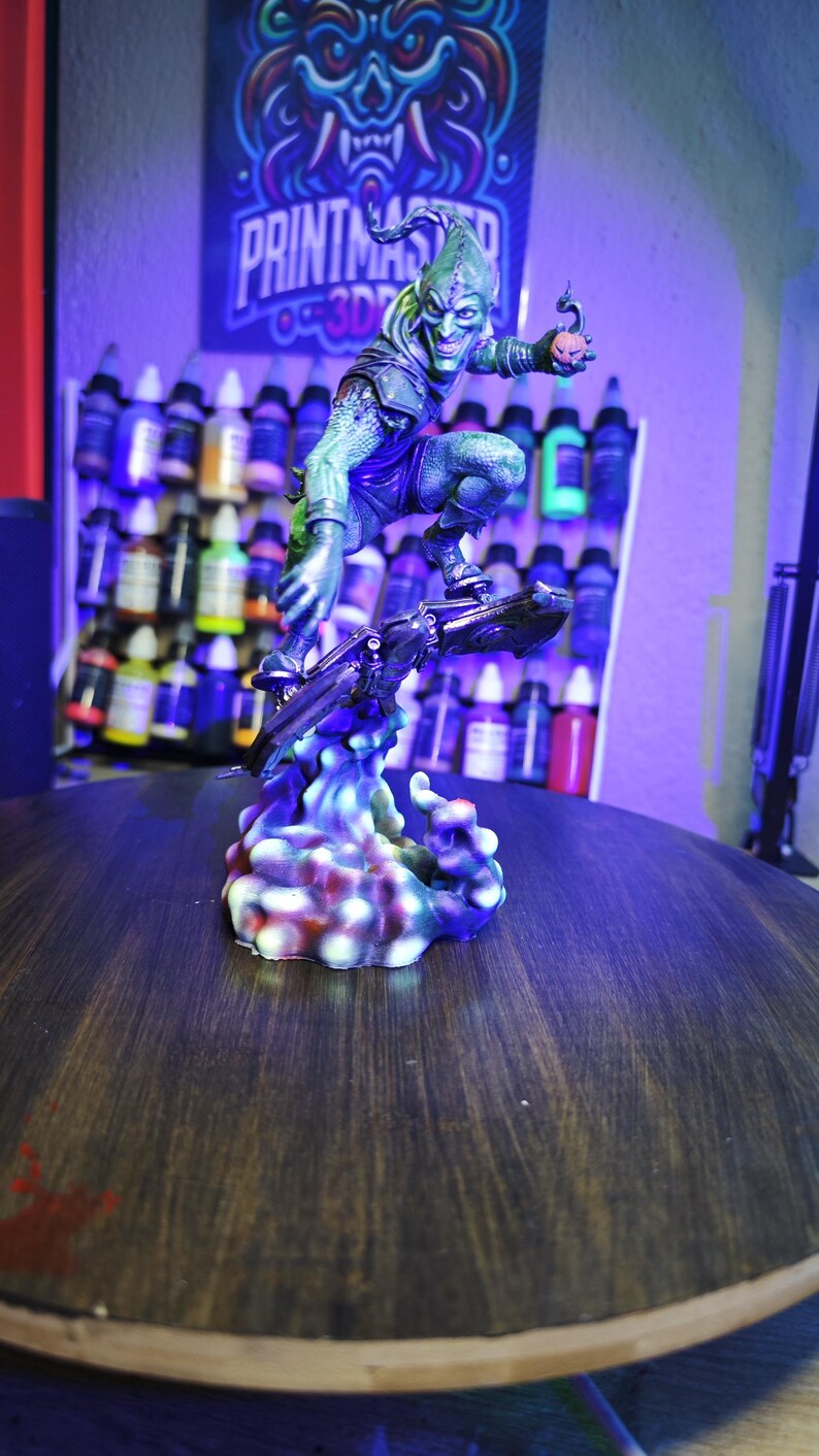Puede incluir: Figura detallada del Duende Verde impresa en 3D, posando en pleno vuelo sobre un planeador, con una bomba de calabaza. La figura est&aacute; pintada en tonos verdes, morados y negros. La base es una nube colorida y estilizada. El fondo presenta un letrero "PRINTMASTER 3D".