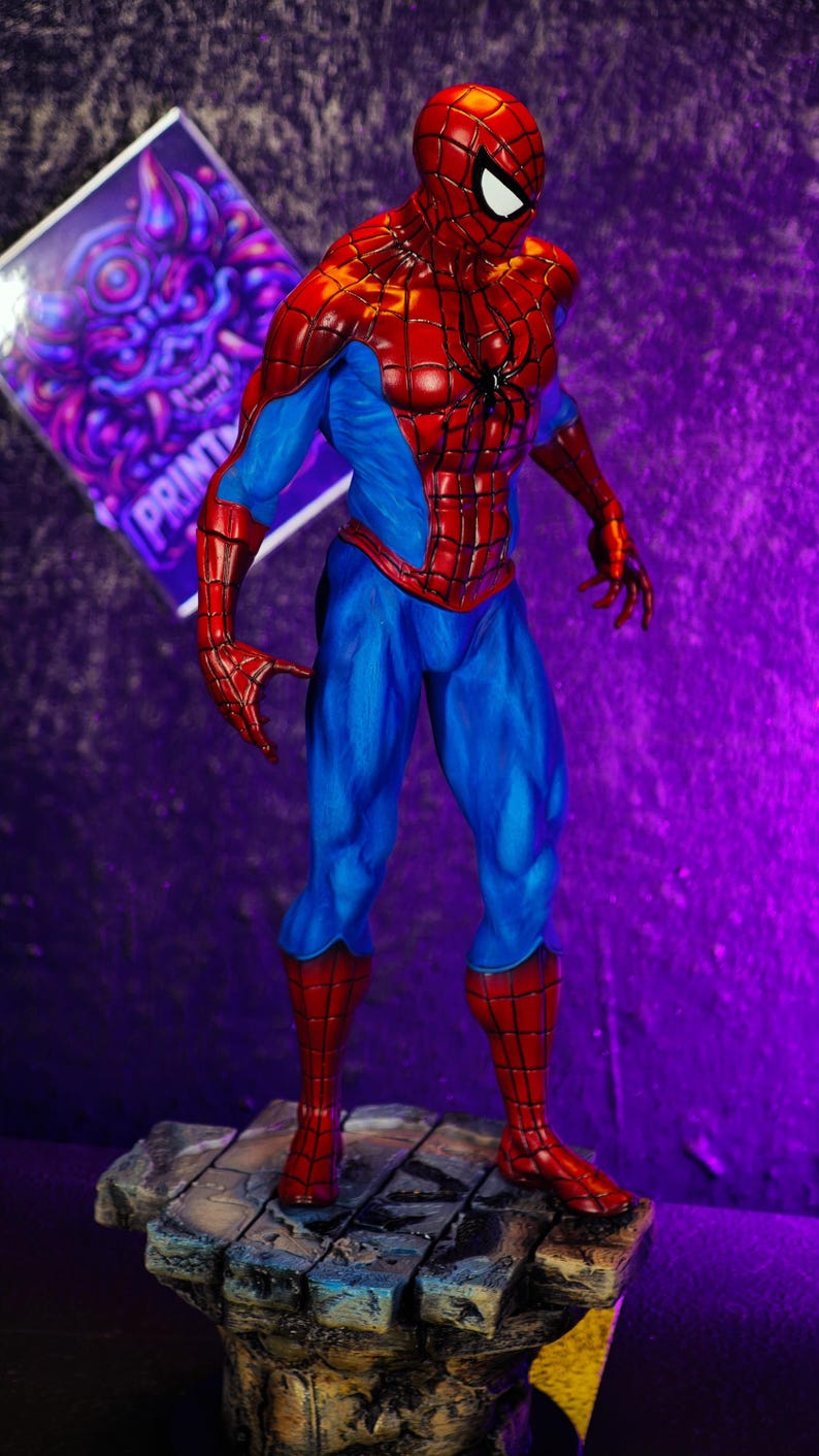 Puede incluir: Figura detallada de Spider-Man con su cl&aacute;sico traje rojo y azul. La figura est&aacute; posada din&aacute;micamente sobre una base texturizada, con un fondo p&uacute;rpura y azul. La figura est&aacute; en una pose din&aacute;mica, con los brazos extendidos.