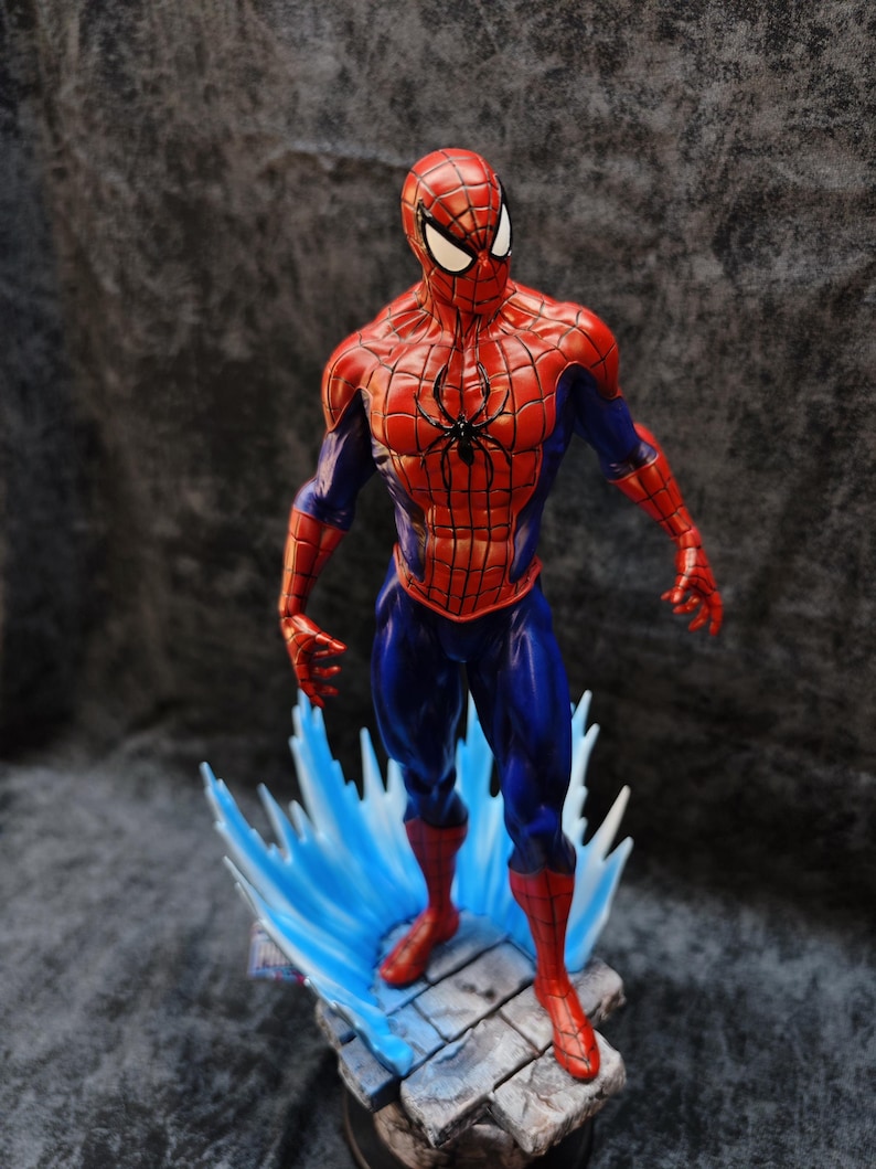 Op de afbeelding: Een gedetailleerd beeldje van Spider-Man in een dynamische pose. De figuur is overwegend rood en blauw, met een zwart spinnenembleem op de borst. Het staat op een voetstuk met blauwe watereffecten, wat het iconische kostuum van de superheld laat zien.