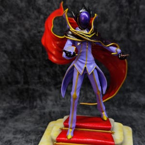 Pu&ograve; includere: Statuetta dettagliata di un personaggio in un completo viola e oro con un mantello rosso. La figura &egrave; su una piattaforma con moquette rossa e finiture dorate. Il personaggio ha un elmo con visiera viola e corona nera.