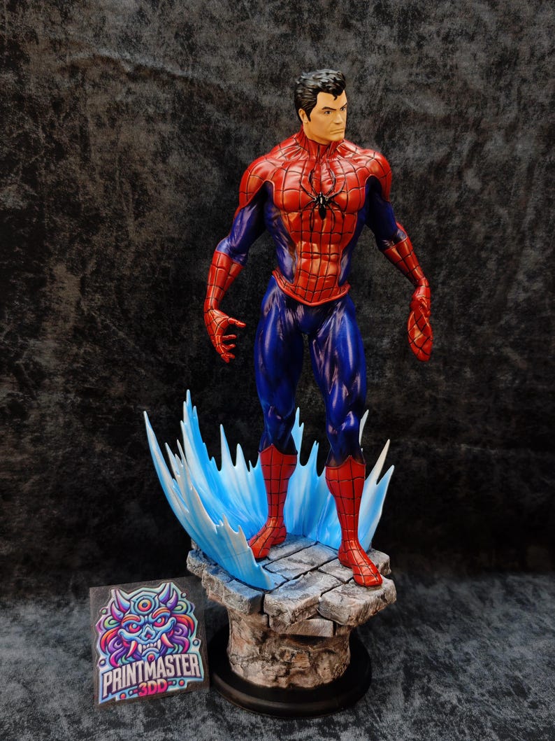 Op de afbeelding: Gedetailleerd beeldje van Spider-Man in een dynamische pose, gekleed in zijn iconische rood-blauwe pak. Het beeld staat op een stenen voet met blauwe watereffecten. De basis heeft een zwarte cirkelvormige standaard. Het beeld heeft een zwart spinnenembleem op de borst.