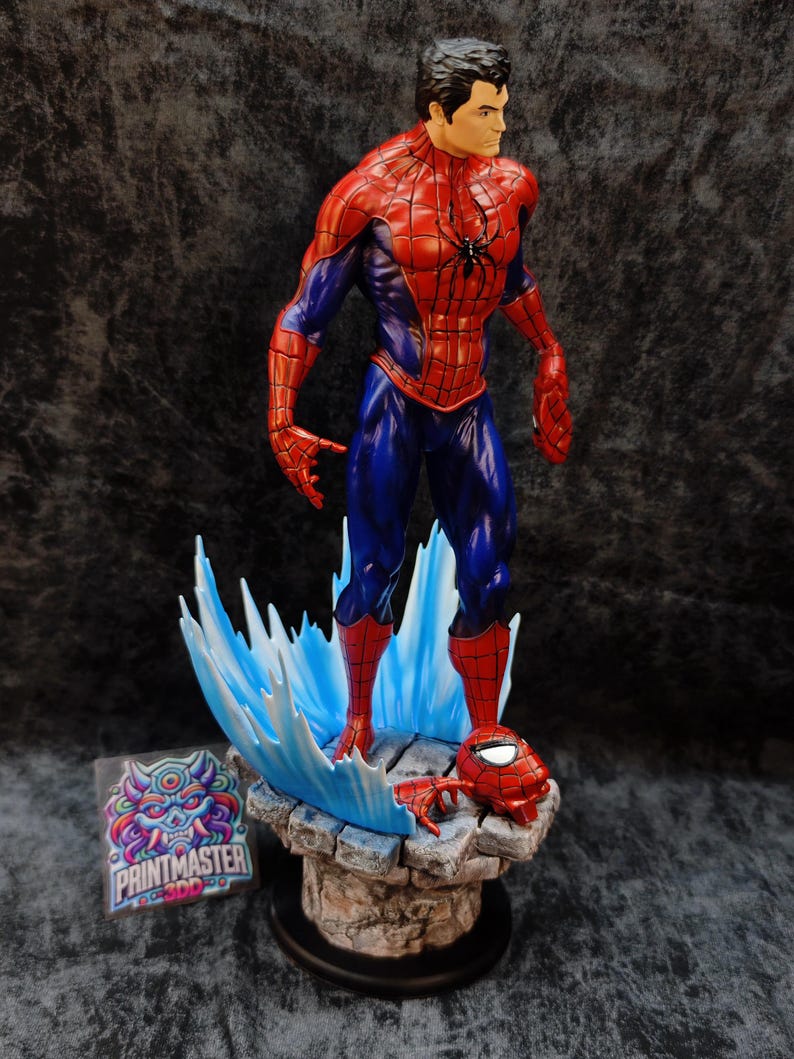 Op de afbeelding: Gedetailleerd beeldje van Spider-Man in een dynamische pose, gekleed in een rood en blauw pak. Het beeld staat op een rotsachtige basis met blauwe watereffecten, en een losgemaakt masker is in de buurt. Zwart spinnenembleem op de borst.