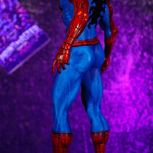 Puede incluir: Figura detallada de Spider-Man, vista desde atr&aacute;s, mostrando su ic&oacute;nico traje rojo y azul. La figura se encuentra sobre una base texturizada con un fondo p&uacute;rpura. El disfraz presenta un emblema de ara&ntilde;a negra en la espalda.