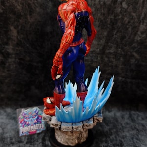 Op de afbeelding: Een gedetailleerd beeldje van Spider-Man in een dynamische pose, gekleed in zijn iconische rood-blauwe pak. Het beeld staat op een getextureerde basis met blauwe watereffecten. Een sticker met de tekst "PRINTMASTER" is zichtbaar.
