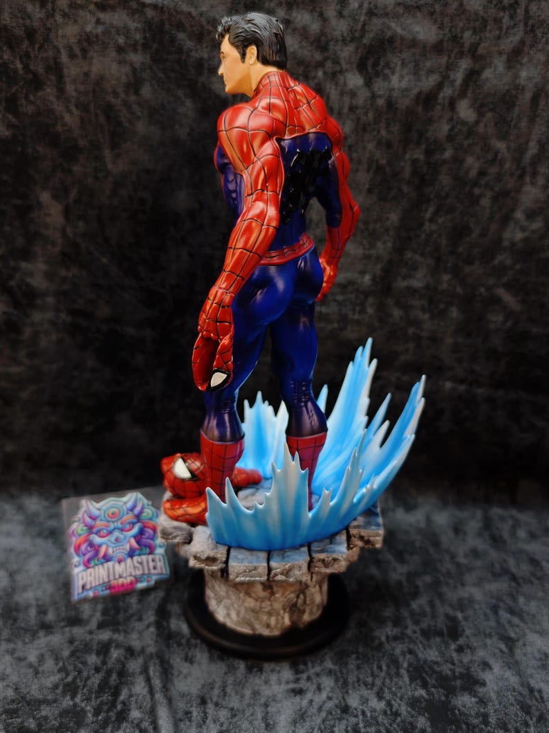 Op de afbeelding: Een gedetailleerd beeldje van Spider-Man in een dynamische pose, gekleed in zijn iconische rood-blauwe pak. Het beeld staat op een getextureerde basis met blauwe watereffecten. Een sticker met de tekst "PRINTMASTER" is zichtbaar.
