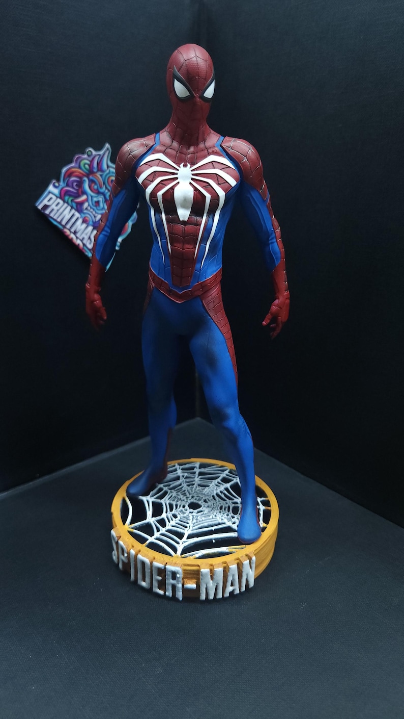 May include: A red and blue Spider-Man action figure stands on a round base with a white spider web design. The base is labeled "SPIDER-MAN".