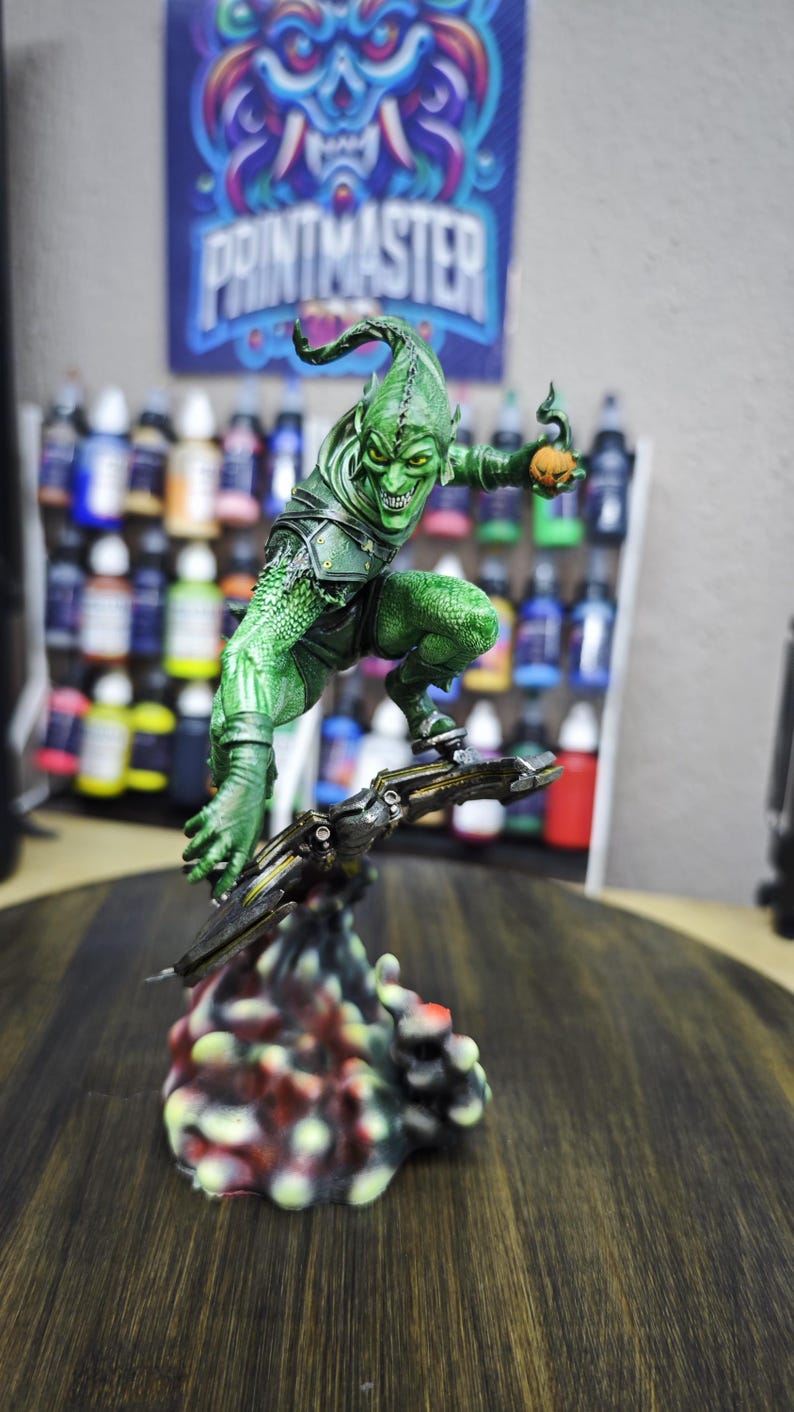 Puede incluir: Una detallada figura del Duende Verde, un villano de c&oacute;mic, en una pose din&aacute;mica. La figura es predominantemente verde con una expresi&oacute;n amenazante, sosteniendo una bomba de calabaza. La base es un dise&ntilde;o colorido y texturizado. Un p&oacute;ster con el texto "PRINTMASTER" est&aacute; en el fondo.