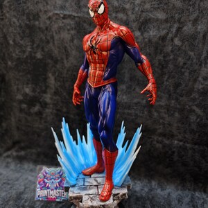 Op de afbeelding: Een gedetailleerd beeldje van Spider-Man in een dynamische pose, gekleed in zijn kenmerkende rood-blauwe pak. Het beeldje staat op een stenen voet met blauwe energie-effecten, met ingewikkelde details en levendige kleuren. De voet heeft de tekst "PRINTMASTER".