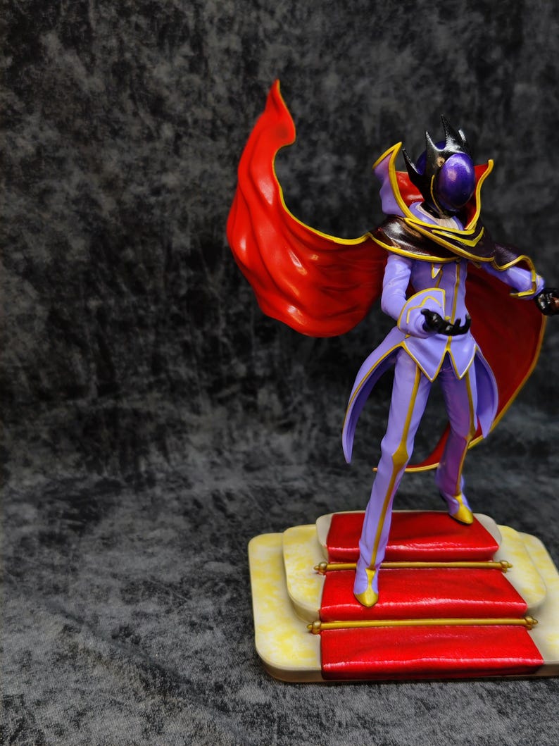 Pu&ograve; includere: Una statuetta di un personaggio in un completo viola e oro con un mantello rosso. La figura &egrave; in piedi su una piccola piattaforma con dettagli rossi e gialli. Il personaggio ha un elmo con una visiera viola.
