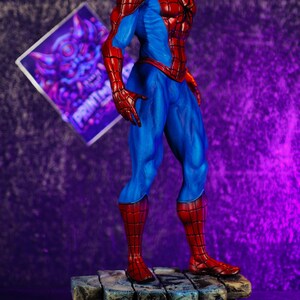 Puede incluir: Una detallada figura de Spider-Man en una pose din&aacute;mica, mostrando su ic&oacute;nico traje rojo y azul. La figura se encuentra sobre una base texturizada, similar a la piedra. El fondo es un degradado de p&uacute;rpura y negro.