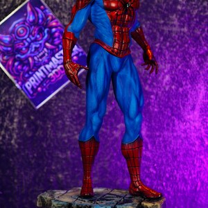 Puede incluir: Una detallada figura de Spider-Man en una pose din&aacute;mica, mostrando su ic&oacute;nico traje rojo y azul. La figura se encuentra sobre una base texturizada, similar a la piedra. Un letrero morado y blanco con el texto "PRINTMAST 300" est&aacute; en el fondo.