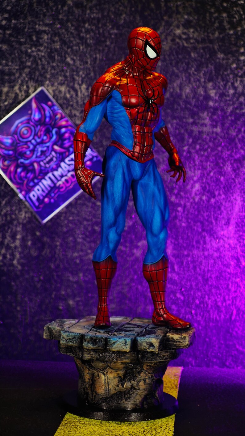Puede incluir: Una detallada figura de Spider-Man en una pose din&aacute;mica, mostrando su ic&oacute;nico traje rojo y azul. La figura se encuentra sobre una base texturizada, similar a la piedra. Un letrero morado y blanco con el texto "PRINTMAST 300" est&aacute; en el fondo.