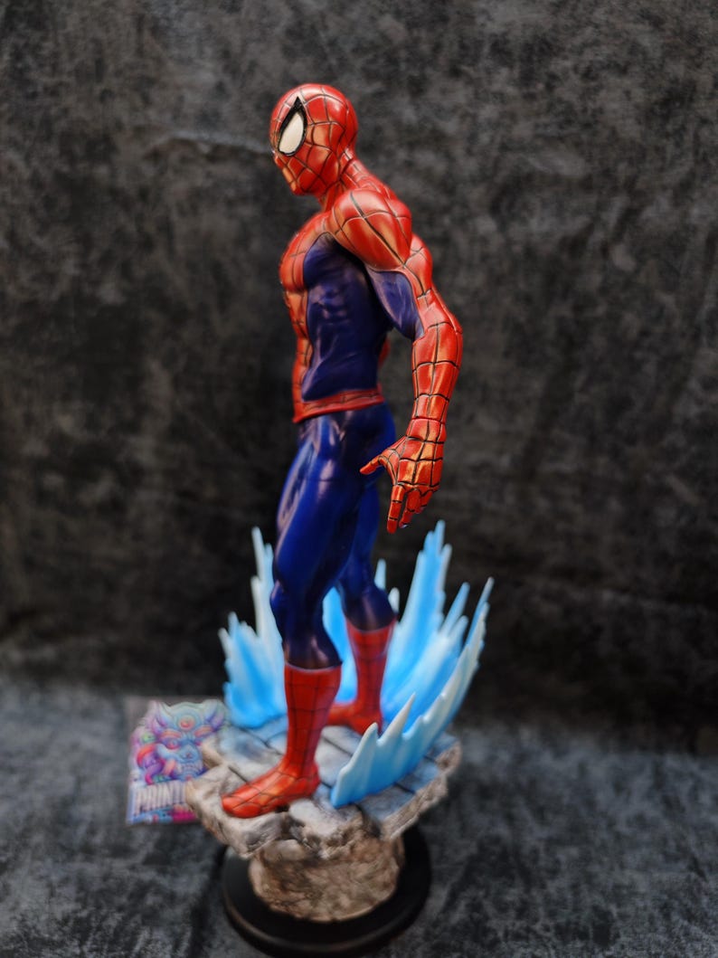 Op de afbeelding: Een gedetailleerd beeldje van Spider-Man in een dynamische pose, met zijn iconische rood-blauwe pak. Het beeldje staat op een rotsachtige basis met blauwe watereffecten. De figuur is ongeveer 20 cm hoog.