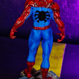 Puede incluir: Figura de acci&oacute;n de Spider-Man, vista desde atr&aacute;s, con un traje azul y rojo. La figura est&aacute; sobre una base detallada, con forma de piedra. El dise&ntilde;o y la pose de la figura son muy detallados.
