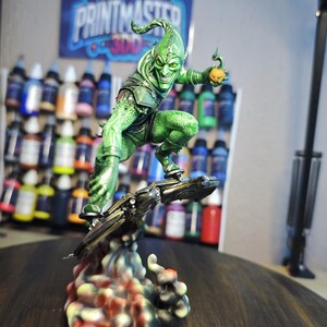 Puede incluir: Una detallada figura del Duende Verde, un villano de c&oacute;mic, montado en un planeador. La figura es predominantemente verde con una bomba de calabaza en la mano. La base es un dise&ntilde;o abstracto y colorido. Un p&oacute;ster con el texto "PRINTMASTER 300" est&aacute; en el fondo.