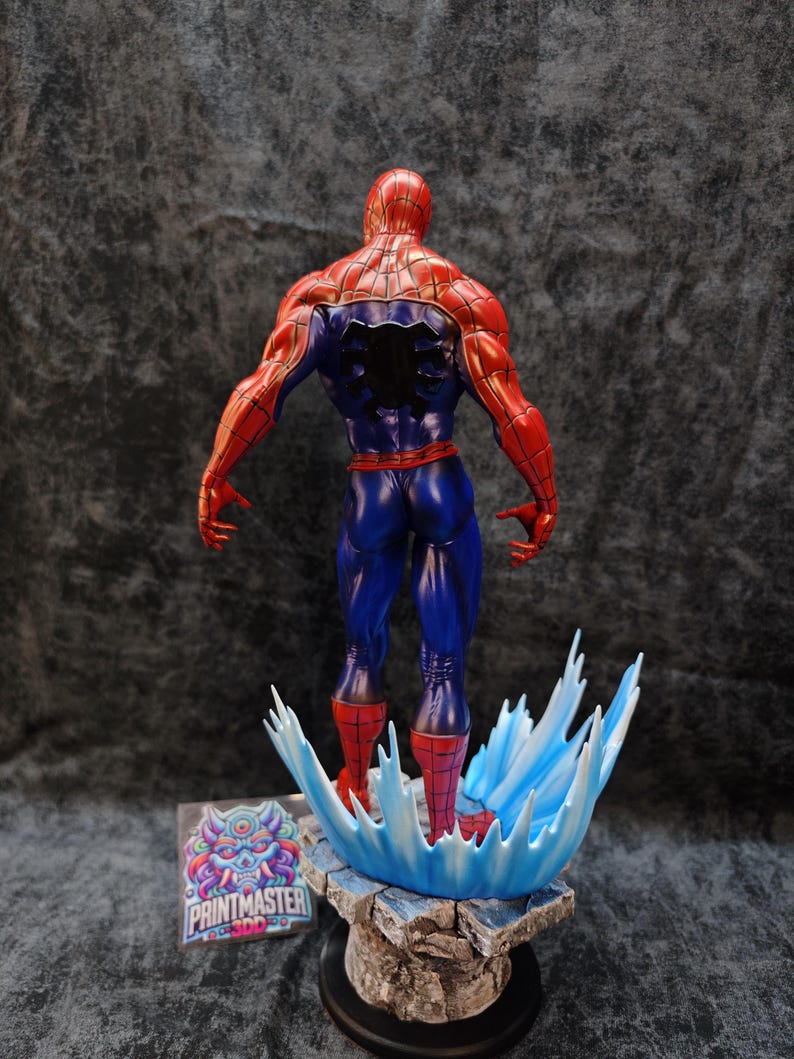 Op de afbeelding: Een gedetailleerd beeldje van Spider-Man, van achteren gezien, met zijn iconische rood-blauwe pak. De figuur staat op een voetstuk met een watereffect, met een logo zichtbaar op de voet. De figuur is ongeveer 30 cm hoog.