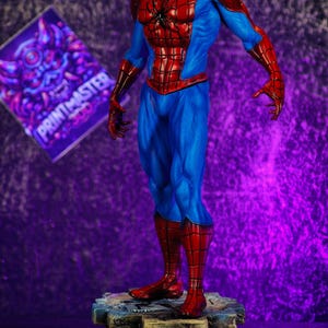 Puede incluir: Una detallada figura de Spider-Man con su cl&aacute;sico traje rojo y azul, de pie sobre una base rocosa. La figura tiene una pose din&aacute;mica, mostrando el dise&ntilde;o ic&oacute;nico del personaje. El fondo es un degradado de morado y negro.