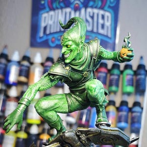 Puede incluir: Una detallada figura del Duende Verde, un villano de c&oacute;mic, en una pose din&aacute;mica sobre un planeador. La figura es predominantemente verde con acentos met&aacute;licos, sosteniendo una bomba de calabaza. El fondo incluye botes de pintura y un p&oacute;ster.