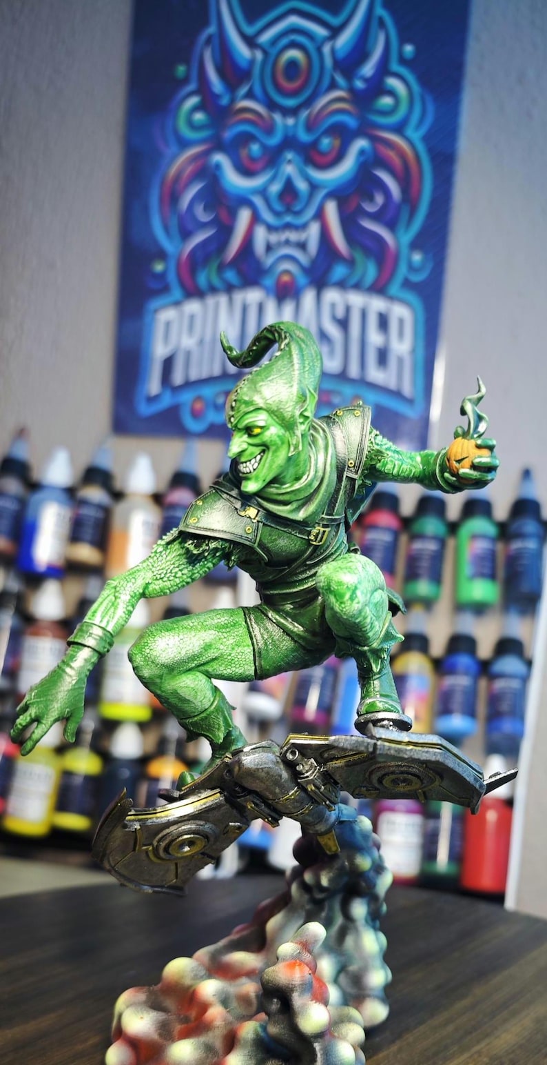Puede incluir: Una detallada figura del Duende Verde, un villano de c&oacute;mic, en una pose din&aacute;mica sobre un planeador. La figura es predominantemente verde con acentos met&aacute;licos, sosteniendo una bomba de calabaza. El fondo incluye botes de pintura y un p&oacute;ster.