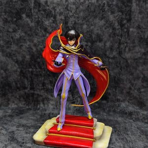 Pu&ograve; includere: Statuetta dettagliata di un personaggio in un completo viola e oro con un mantello rosso fluente. La figura &egrave; su una piattaforma con tappeto rosso con dettagli dorati. Il personaggio ha i capelli neri ed &egrave; in posa dinamica.