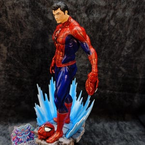 Op de afbeelding: Gedetailleerd beeldje van Spider-Man in een dynamische pose, met een rood en blauw kostuum. Het beeldje staat op een rotsachtige basis met blauwe energie-effecten en bevat een losgemaakt masker. Het Printmaster-logo is zichtbaar.