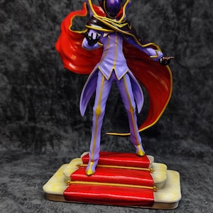 Pu&ograve; includere: Statuetta dettagliata di un personaggio in un completo viola e oro con un mantello rosso. La figura &egrave; su una piattaforma con moquette rossa con finiture dorate. Il personaggio ha un elmo e tiene in mano un piccolo oggetto.