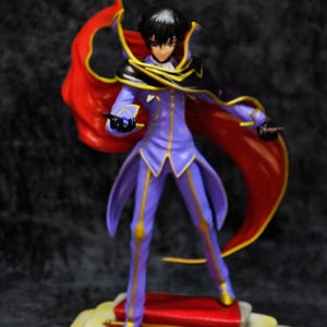 Pu&ograve; includere: Statuetta di un personaggio in un completo viola e oro con un mantello rosso. La figura &egrave; in piedi su una piattaforma con tappeto rosso e finiture dorate. Il personaggio ha i capelli neri ed &egrave; in posa dinamica.