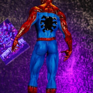 Puede incluir: Figura detallada de Spider-Man, vista desde atr&aacute;s. La figura lleva un cl&aacute;sico traje rojo y azul con un emblema de ara&ntilde;a negro en la espalda. La figura est&aacute; sobre una base de piedra.