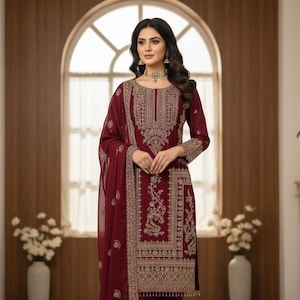 May include: A burgundy embroidered formal dress with a matching scarf. The dress features intricate gold threadwork around the neckline, sleeves, and hem. The outfit is worn with gold jewelry and is suitable for special occasions.