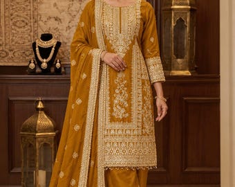 Può includere: Un completo a tre pezzi color giallo senape composto da una tunica a maniche lunghe, pantaloni ampi abbinati e una dupatta coordinata. I capi sono riccamente decorati con elaborati ricami floreali e perline bianche e dorate.