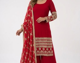 May include: A red salwar kameez ensemble featuring a long-sleeved tunic with gold embroidery on the sleeves and hem, paired with wide-leg pants. A matching red dupatta with gold detailing completes the outfit. The outfit is worn by a person.