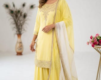 May include: A light yellow Indian salwar kameez ensemble. The outfit features a long tunic with intricate embroidery and wide-leg pants. A white dupatta with gold trim completes the look. The outfit is made of a lightweight fabric.