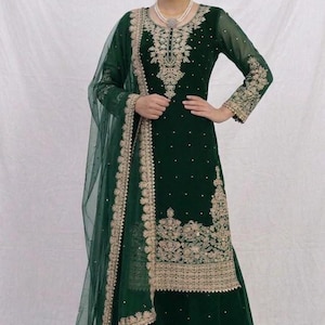 May include: A dark green, long-sleeved salwar kameez with intricate gold embroidery and embellishments. The ensemble includes a matching dupatta and wide-leg pants. The outfit is adorned with small, sparkling details.