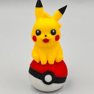 May include: A yellow Pikachu figure with black-tipped ears, red cheeks, and a red mouth, perched atop a red, white, and black Poké Ball. The figure is a 3D-printed collectible, showcasing a popular character from the Pokémon franchise.