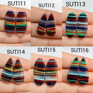 Op de afbeelding: Zes paren cabochons gelabeld SUTI11 tot en met SUTI16, elk met horizontale strepen in diverse kleuren zoals blauw, rood, oranje, groen en zwart. De vormen wisselen af tussen ovaal en druppelvorm, met een gladde, gepolijste afwerking.