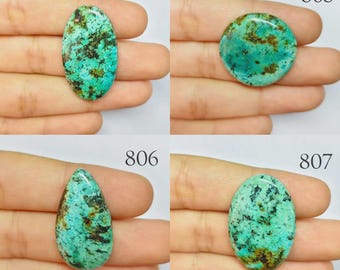 May include: Four turquoise gemstones in various shapes: oval, round, teardrop, and oval. Each stone has a mottled pattern of teal and brown. The gemstones are held in a hand, with the numbers 804, 805, 806, and 807 visible.