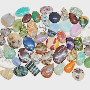 Può includere: Una collezione di pietre preziose lucide di varie forme e colori, tra cui ovali, a goccia e irregolari. Le pietre presentano una gamma di tonalità, come verde, blu, marrone e viola, con motivi e texture unici.
