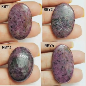 May include: Four oval gemstones in shades of purple, grey, and black. Each stone displays a unique pattern and texture, with varying colour intensity. The gemstones are presented against a light background.
