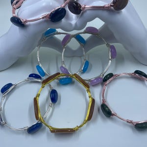 Puede incluir: Cinco pulseras envueltas en alambre con cuentas de vidrio de diferentes colores. Las pulseras están hechas con alambre de cobre, plata y oro.