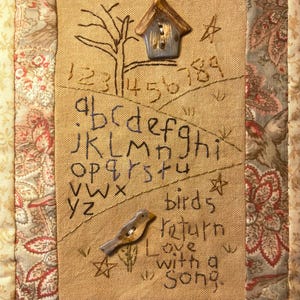 May include: A handcrafted textile art piece with a birdhouse, tree, and bird embellishments. The artwork features embroidered letters, numbers, and the words "birds return Love with a Song." The piece is framed with floral patterned fabric.