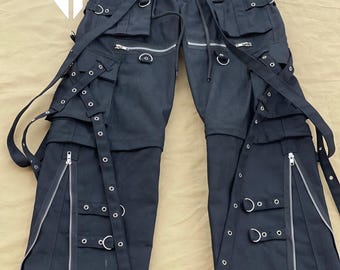 May include: Black cargo pants with multiple straps, buckles, and zippers. The pants have a utilitarian style with a lot of pockets and hardware.