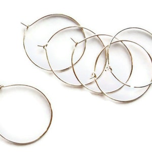 Peut inclure: Cinq boucles d'oreilles créoles argentées de différentes tailles, disposées en demi-cercle sur un fond blanc.